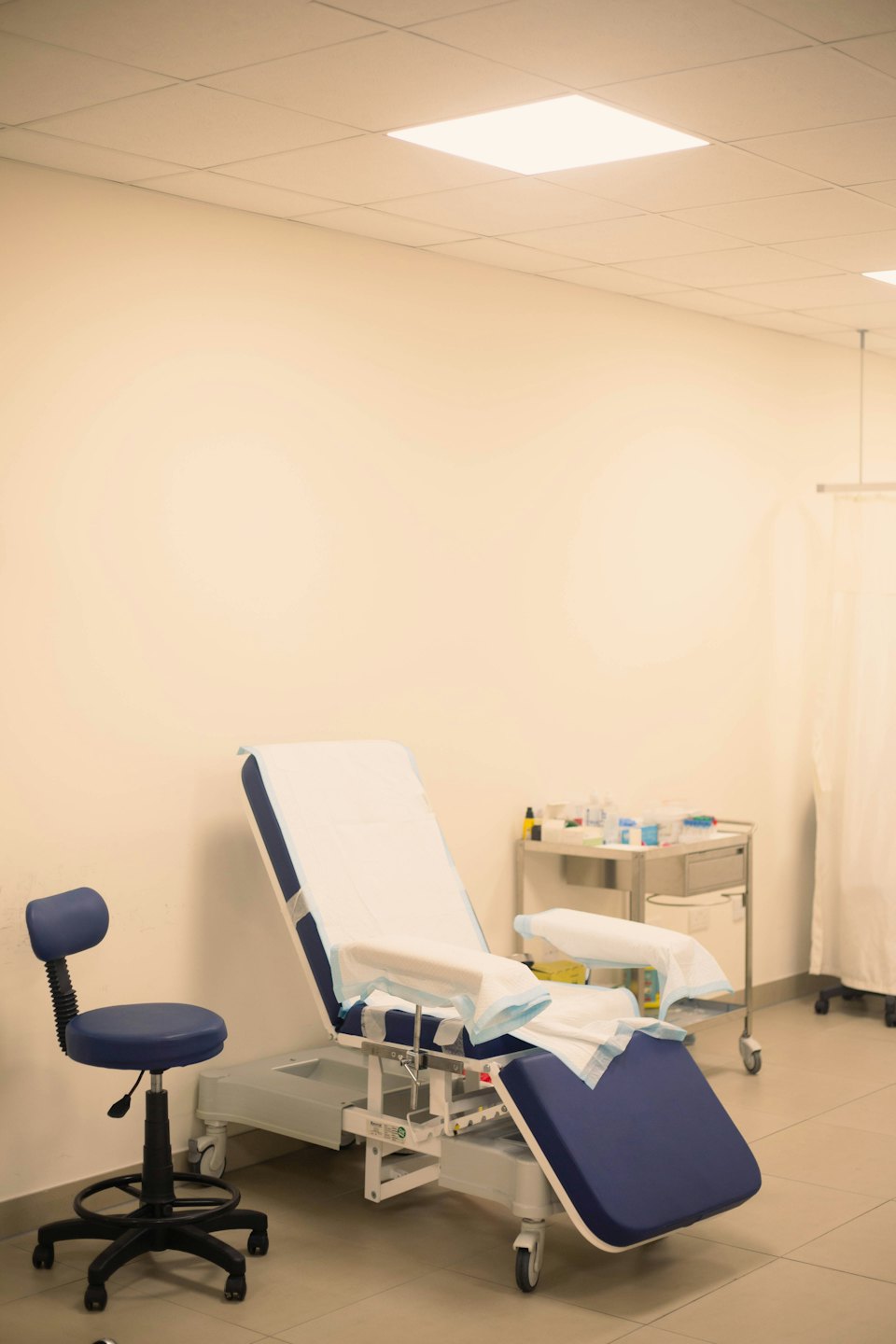 Stanza medica vuota con sedia e carrello blu e bianchi.