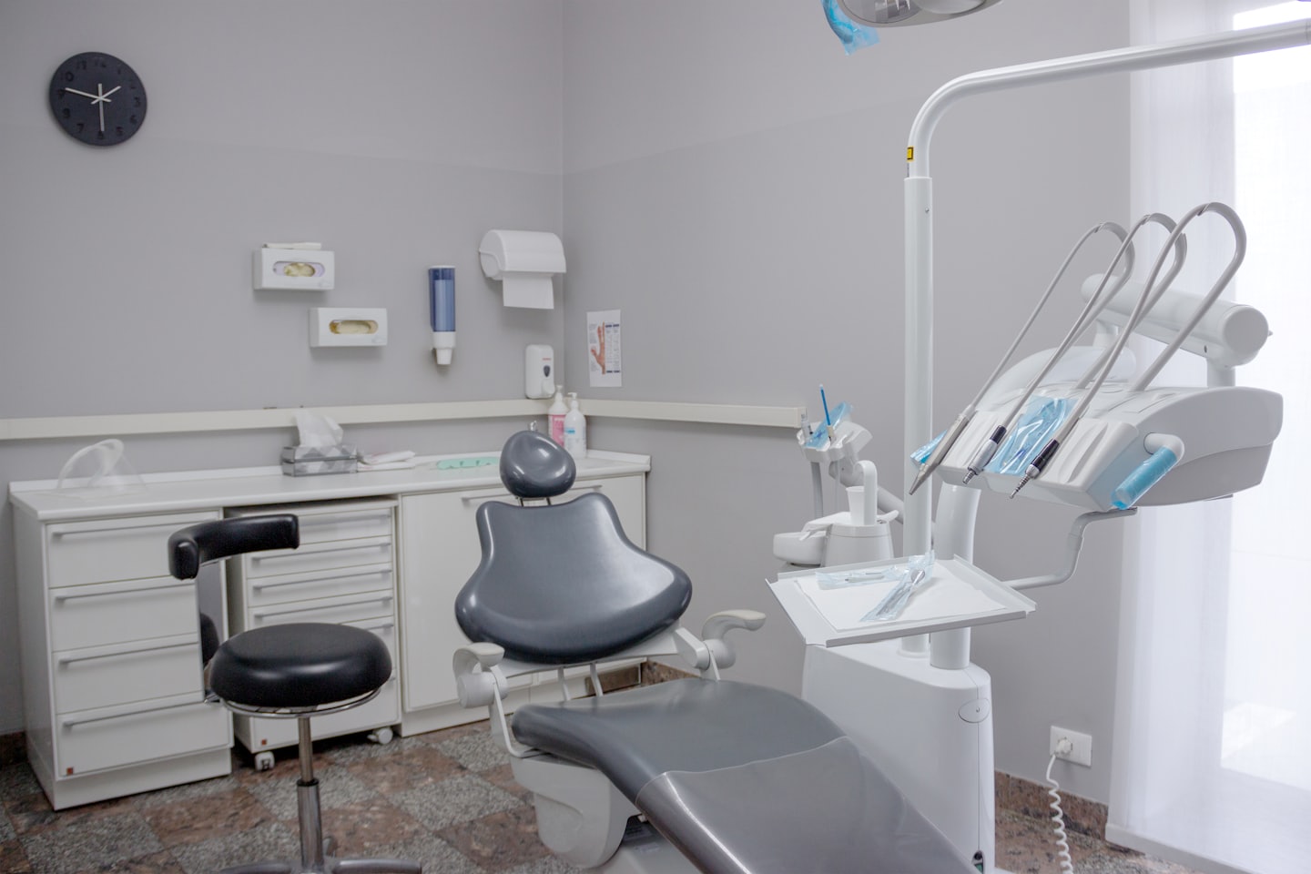 Moderna sala d'esame dentistico vuota con sedia grigia e attrezzature bianche.